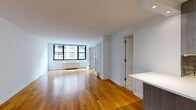 Located at 315 West 57th Street in Midtown Manhattan, this one-bedroom, one-bathroom residence offers a well-designed layout across a single floor. Warm hardwood flooring runs throughout the main living areas and bedroom, lending a cohesive and inviting character to the space.

The open living area is bright and airy, benefiting from large black-framed windows that allow natural light to fill the room and offer views of the surrounding cityscape. The space flows naturally from the entry into the living area, providing a comfortable and functional arrangement.

The kitchen is modern and efficiently designed, featuring grey wood-grain cabinetry, a mosaic tile backsplash, stainless steel appliances including a full-size refrigerator, and a white stone peninsula countertop that doubles as a breakfast bar. The kitchen transitions seamlessly into the living space, making it ideal for everyday use and entertaining.

The bedroom is generously proportioned, featuring the same rich hardwood flooring, a large window with an urban view, and a built-in closet with shelving for ample storage.

The bathroom is finished to a high standard, with marble-style floor and wall tiles, a soaking tub with a glass sliding enclosure, a wall-mounted wood vanity with an integrated white sink, and a large mirror above. The overall aesthetic is clean, contemporary, and well-appointed throughout.