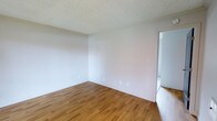 This single-floor unit offers a straightforward and functional layout, designed to maximize comfort and usability. The interior is finished with warm-toned hardwood flooring throughout, lending a classic and inviting feel to the living space. Walls are painted in a crisp, neutral white, creating a bright and airy atmosphere that allows for versatile furnishing and décor options. The textured ceiling adds a subtle architectural detail consistent throughout the unit. The bedroom is a well-proportioned, open room bathed in natural light, with clean white walls and the same hardwood flooring continuing seamlessly from the main living areas. A doorway connects the spaces with ease, supporting a smooth and logical flow through the unit. The overall design is clean and understated, appealing to those who value simplicity and practicality. With one bedroom and one bathroom, this unit is ideally suited for an individual or couple seeking a comfortable, low-maintenance living environment. The neutral palette and quality flooring provide a solid foundation for personalizing the space to suit any lifestyle.
