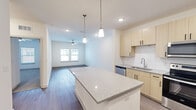 This thoughtfully designed 1-bedroom, 1-bathroom residence offers a clean, modern aesthetic across a single floor. The open-concept kitchen and living area forms the heart of the home, where wood-look flooring, recessed lighting, and a ceiling fan create a bright and comfortable atmosphere. The kitchen is well-appointed with light wood cabinetry featuring matte black hardware, granite-look countertops, a central island with pendant lighting, and a full suite of stainless steel appliances including a French door refrigerator, electric range, over-the-range microwave, and dishwasher. The living area extends naturally from the kitchen, benefiting from natural light through a window and ample open floor space. The bedroom is generously sized, featuring soft carpet flooring, a ceiling fan, and a window that fills the room with natural light. A dedicated walk-in closet with wire shelving provides practical storage. The in-unit laundry room houses a full-size washer and dryer with additional wire shelving above. The bathroom includes wood-look flooring, a soaking tub, grab bars, and a vanity with granite-look countertops, rounding out this functional and modern living space.