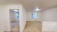 Located at 6940 37th Ave S in Seattle's Brighton neighborhood, this one-bedroom, one-bathroom unit offers a thoughtfully organized single-floor layout. The living area features neutral-toned carpet and white walls, with windows that bring in natural light and offer views of surrounding greenery. The space flows openly between the living room and kitchen, making efficient use of the floor plan.

The kitchen is equipped with light wood cabinetry, a white electric range, refrigerator, microwave, and a single-basin sink, all set on wood-look flooring. The layout follows an L-shaped configuration that maximizes counter and storage space.

The bedroom is a comfortable, carpeted room with a large window overlooking trees, providing a calm, natural atmosphere. A built-in closet with bifold doors and integrated shelving offers practical storage. The room is bright and simply finished with clean white walls.

The bathroom features wood-look flooring, a full bathtub/shower combo, toilet, and vanity with sink. Accessibility is a notable feature, with stainless steel grab bars installed along the walls. A small window provides ventilation and light.

Overall, this unit presents a clean, functional design with consistent finishes throughout, suited for those seeking a practical and well-lit living space in Seattle.