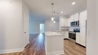 This Premier 2-bedroom, 2-bathroom home in Spring Hill, TN offers a well-designed single-level layout with a bright, open feel throughout. The kitchen serves as the heart of the home, featuring white shaker cabinetry, granite countertops, a tile backsplash, stainless steel appliances including a refrigerator with ice maker and built-in microwave, and a central island with pendant lighting and an undermount sink — perfect for both cooking and casual dining. Rich hardwood-style flooring flows through the kitchen and common areas, transitioning to plush carpet in the living and bedroom spaces. The spacious living room is bathed in natural light from large windows and a glass door that opens to outdoor views of the community. Both bedrooms are generously sized, each with ceiling fans, ample natural light, and access to well-organized closets with wire shelving systems. The bathrooms are finished with granite-topped white vanities, tile flooring, and clean, neutral aesthetics. A dedicated laundry room with a full-size washer and dryer adds everyday convenience. Neutral tones and consistent finishes throughout give the space a cohesive, move-in-ready appeal.