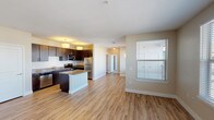 Located at 250 Summit Blvd in Broomfield, Colorado, this single-floor residence offers a well-designed open-concept layout that seamlessly connects the kitchen, dining, and living areas. The kitchen is a standout feature, equipped with rich dark espresso cabinetry, stainless steel appliances including a refrigerator, range, microwave, and dishwasher, and a central island with a neutral-toned countertop that provides additional prep and seating space. Pendant lighting above the island and flush-mount ceiling fixtures add a warm, functional glow to the space. Light hardwood-style flooring flows throughout the main living areas, complementing the neutral wall tones and creating a bright, cohesive aesthetic. The living area is generously proportioned, bathed in natural light from multiple large windows fitted with blinds, and offers access to an outdoor balcony. The bedroom features plush carpet, a ceiling fan, a walk-in closet, and direct access to the bathroom. The bathroom is appointed with dark vanity cabinetry, a wide countertop, a large framed mirror with lighted vanity fixtures, and tile surround detailing. Overall, the space presents a clean, contemporary design well-suited to comfortable everyday living.