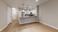 This single-floor unit offers a thoughtfully designed open-concept layout that maximizes both functionality and comfort. The kitchen serves as the centerpiece of the living space, showcasing crisp white shaker-style cabinetry, dark laminate countertops, and a full suite of stainless steel appliances including a refrigerator, electric range, over-the-range microwave, and dishwasher. A peninsula island with pendant lighting overhead provides additional counter space and a natural visual divide between the kitchen and the adjacent living area. Track lighting throughout the kitchen ensures excellent illumination. Light-toned luxury vinyl plank flooring spans the open living and kitchen areas, lending a clean and contemporary feel. The bedroom is generously sized and features soft, neutral carpeting, warm-toned walls, and a wide bank of windows fitted with horizontal blinds that invite ample natural light while maintaining privacy. A ceiling fan adds year-round comfort to the room. The bathroom is well-appointed with white cabinetry, a rich dark-toned countertop, a backlit vanity mirror, and a full soaking tub with a shower combination set against clean white surround panels. Tile flooring in the bathroom complements the neutral palette carried throughout the entire space, creating a cohesive and move-in-ready home.