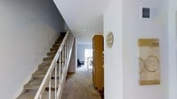 This two-story residence offers a thoughtfully designed layout that balances comfort and functionality across both levels. The entryway serves as the central hub of the home, immediately revealing the open flow between spaces. A classic staircase with white-painted wood railings and carpeted treads rises prominently from the entry, providing a clean and traditional aesthetic while connecting the two floors with ease.

The main level features neutral-toned carpeting that extends into the living areas, lending a warm and cohesive feel throughout. The hallway leading from the entry opens toward a bright living space, where natural light filters through a sliding glass door or large window, illuminating the room and creating an inviting atmosphere. Adjacent to the entry, warm wood-toned cabinetry adds both storage and visual warmth to the space.

The overall color palette is understated and neutral, with crisp white walls, soft gray accents, and natural wood tones working together to create a calm, livable environment. The recessed lighting and clean ceiling lines contribute to a tidy, well-maintained interior. The combination of practical storage solutions, open sightlines, and multi-level living makes this a versatile and comfortable home suited for a variety of lifestyles.