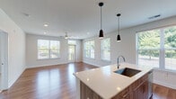 This contemporary single-floor residence is designed with a clean, modern aesthetic and a thoughtful open-concept layout. The spacious living area is bathed in natural light from multiple large windows fitted with blinds, and features polished hardwood flooring, recessed lighting, a ceiling fan, and direct access to a private balcony with outdoor views of surrounding greenery.

The kitchen is seamlessly integrated into the living space and showcases light wood grain cabinetry extending to the ceiling for ample storage, white quartz countertops, a subway tile backsplash, and a full suite of stainless steel appliances including a refrigerator with ice maker, electric range, and over-the-range microwave. A central island with an undermount sink and stylish pendant lighting overhead serves as both a functional workspace and a visual focal point.

The bedroom is generously sized with plush carpeting, a large window offering outdoor views, and access to a walk-in closet. Two bathrooms serve the unit — one featuring a soaking tub and wood-toned vanity cabinetry, and a second en-suite bathroom with a glass-enclosed walk-in shower, dual-sink vanity with white countertops, and hardwood-style flooring. The overall palette of soft whites and warm wood tones creates a cohesive, welcoming ambiance throughout.