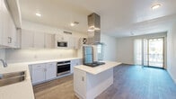 This well-designed 2-bedroom, 3-bathroom single-floor residence offers a thoughtfully laid-out living space that balances modern style with everyday functionality. The open-concept kitchen serves as the heart of the home, showcasing crisp white shaker cabinetry, a subway tile backsplash, gleaming stone countertops, and a full suite of stainless steel appliances including a gas cooktop, wall oven, built-in microwave, and refrigerator. A central island with a gas range and a striking stainless steel hood vent anchors the kitchen, which flows seamlessly into the living area. Light wood-style flooring runs throughout the main living spaces, while large sliding glass doors invite natural light and provide access to an outdoor area. Both bedrooms are carpeted and generously proportioned, each featuring ceiling fans and large windows with blinds that frame outdoor views. The spacious primary bedroom includes ample closet space. The three bathrooms are finished with stone-look countertops and clean, contemporary fixtures; one features a sleek walk-in shower with a backlit vanity mirror, while another offers a full soaking tub and shower combination. A dedicated closet completes the layout, adding practical storage to this modern and move-in-ready residence.