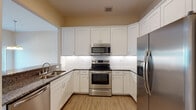 This two-story residence in New Port Richey, Florida offers a well-designed layout with modern finishes throughout. The kitchen is a standout feature, showcasing white shaker-style cabinetry, dark granite countertops, a textured subway tile backsplash, and a full suite of stainless steel appliances including a range, over-the-range microwave, dishwasher, and French door refrigerator, all set atop durable wood-look flooring. The open living and dining area is bright and airy, with soaring vaulted ceilings, recessed lighting, a ceiling fan, and sliding glass doors that open to a private balcony, allowing an abundance of natural light to fill the space. The staircase connects both floors seamlessly, with a large closet providing ample storage near the entry level. Bedrooms feature wood-look or plush carpeted flooring, ceiling fans, and generous natural light from well-positioned windows. The bathrooms are thoughtfully appointed — one includes a subway-tiled tub and shower combination with a quartz-topped vanity, while another features a dual-sink vanity, a framed glass walk-in shower, and elegant tile flooring. The overall aesthetic is clean, neutral, and move-in ready, offering a comfortable and functional living environment.