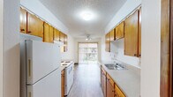 Located at 10450 SW McDonald St. in Tigard, Oregon, this single-floor, one-bedroom, one-bathroom residence offers a practical and well-organized layout. The galley-style kitchen is a standout feature, lined on both sides with warm wood cabinetry offering generous storage, complemented by light-toned countertops and white appliances including a refrigerator and electric range. Wood-look flooring runs throughout the kitchen and living areas, adding a clean, cohesive feel. The kitchen flows naturally into a dining and living area brightened by a sliding glass door that opens to an outdoor view, fitted with vertical blinds and a ceiling fan with integrated lighting overhead. Baseboard heating is present throughout the unit. The bedroom is a comfortable, quiet retreat featuring plush carpeting, a window that invites natural light, and a sliding-door closet with warm wood paneling providing ample storage. The bathroom is accessed through wood-framed doors and features a vanity with matching cabinetry, a single sink with light countertops, and a full-length mirror. A textured ceiling is consistent throughout the unit, contributing to its classic residential character. This thoughtfully laid-out home offers functional living in a convenient Tigard location.