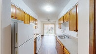 Located at 10450 SW McDonald St. in Tigard, Oregon, this single-floor, one-bedroom, one-bathroom residence offers a practical and well-organized layout. The galley-style kitchen is a standout feature, lined on both sides with warm wood cabinetry offering generous storage, complemented by light-toned countertops and white appliances including a refrigerator and electric range. Wood-look flooring runs throughout the kitchen and living areas, adding a clean, cohesive feel. The kitchen flows naturally into a dining and living area brightened by a sliding glass door that opens to an outdoor view, fitted with vertical blinds and a ceiling fan with integrated lighting overhead. Baseboard heating is present throughout the unit. The bedroom is a comfortable, quiet retreat featuring plush carpeting, a window that invites natural light, and a sliding-door closet with warm wood paneling providing ample storage. The bathroom is accessed through wood-framed doors and features a vanity with matching cabinetry, a single sink with light countertops, and a full-length mirror. A textured ceiling is consistent throughout the unit, contributing to its classic residential character. This thoughtfully laid-out home offers functional living in a convenient Tigard location.