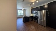 Located at 200 W Civic Center Dr in Sandy, UT, this 490-square-foot single-floor apartment offers a well-designed layout that maximizes every inch of available space. The open-concept kitchen is a standout feature, equipped with dark espresso cabinetry, a mosaic tile backsplash, granite countertops, and a full suite of stainless steel appliances including a refrigerator, electric range, built-in microwave, and dishwasher. A peninsula with an undermount sink and additional seating space serves as the natural divider between the kitchen and the main living area. Rich, dark hardwood-style flooring runs throughout the living spaces, adding warmth and cohesion to the unit. The main room features a ceiling fan and a window that brings in natural light. A distinctive sliding barn door leads to the closet, adding a modern, space-saving design element. The full bathroom is finished with large-format light gray wall and floor tiles, a soaking tub with a curved shower curtain rod, a granite-topped vanity with dark cabinetry, and overhead storage. Track lighting in the kitchen and neutral wall tones throughout contribute to a clean, contemporary aesthetic.