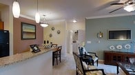Located at 1150 Baxter Lane in Knightdale, NC, this single-floor residence offers a well-designed, open-concept living space that balances comfort and style. Crown molding throughout adds a refined architectural detail, lending the interior a polished, cohesive feel.

The living and dining areas flow seamlessly together, creating an inviting, connected atmosphere. A granite-topped breakfast bar serves as a natural divider between the kitchen and dining space, offering casual seating alongside a dedicated dining area illuminated by a stylish pendant light fixture. The soft, neutral carpet in the living area provides warmth underfoot, while the muted sage and warm beige wall tones contribute to a calm, welcoming ambiance.

Decorative wall accents, including sunburst mirrors and framed artwork, add character without overwhelming the space. The sitting area is furnished with patterned upholstered chairs and a round accent table, creating an intimate nook for relaxing or entertaining.

A glimpse into the utility area reveals an in-unit washer and dryer, a highly practical feature. Closet storage is also visible, suggesting thoughtful use of available space throughout this efficiently designed single-level home.
