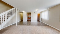 Located on Main Street in West Haven, Connecticut, this two-story home offers a well-distributed layout across two floors. The main level features a combined kitchen and living room area, where warm-toned hardwood-style flooring flows through the kitchen. The kitchen is equipped with rich oak cabinetry, dark countertops, a gas range, dishwasher, and full-size refrigerator, with louvered closet doors providing additional storage. The living room extends generously from the kitchen, with plush carpeting and large windows fitted with vertical blinds that allow abundant natural light to fill the space. A white-railed staircase connects the main level to the upper floor. Upstairs, the spacious bedroom features carpet flooring, neutral-toned walls, and a drop ceiling. A versatile additional room on this level, also carpeted and featuring a drop ceiling, offers flexible use as an office or secondary living area with louvered closet doors. The full bathroom includes a tub/shower combination, a white vanity with brushed nickel hardware, and wood-look tile flooring. Throughout the home, a neutral color palette of warm beige tones creates a cohesive and inviting atmosphere.