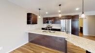 Located in Grand Forks, North Dakota, this single-floor residence offers a thoughtfully designed open-concept layout with contemporary finishes throughout. The kitchen serves as the heart of the home, showcasing rich dark cabinetry, stainless steel appliances — including a refrigerator with ice maker, microwave, and range — and a generous granite-topped island with a built-in sink and pendant lighting overhead. Light wood-tone flooring flows seamlessly from the kitchen into the spacious living area, which is filled with natural light through large windows and a sliding glass door leading to an outdoor patio. The bedrooms feature plush carpeting and well-sized windows that bring in natural daylight. The bathrooms are finished with dark vanity cabinetry, light countertops, and chrome fixtures; one bath includes a walk-in shower, while another features a well-lit vanity with ample storage. A dedicated laundry room houses a full-size washer and dryer with dark overhead cabinetry for additional storage. A clean, wide hallway with wood-look flooring connects the private spaces, maintaining a cohesive aesthetic throughout. The overall ambiance is bright, clean, and move-in ready, offering a comfortable and functional living environment.