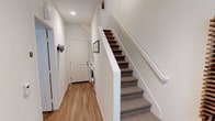 This multi-story residence spans three floors, offering a functional and well-designed layout throughout. The entry level features warm hardwood-style flooring, a convenient in-unit stacked washer and dryer tucked neatly beneath the staircase, and a framed art piece that adds a welcoming touch. Carpeted stairs with a clean white handrail connect the levels seamlessly.

The main living area is bright and inviting, with large windows dressed in horizontal blinds that allow generous natural light to fill the space. A ceiling fan adds comfort, and the open feel makes it ideal for relaxing. Adjacent to this is a dining area accented by a warm gold pendant light and colorful wall art, creating an energetic and casual atmosphere.

The kitchen is well-equipped with rich wood cabinetry, light countertops, a light blue tile backsplash, and stainless steel appliances including a range, microwave, and double-basin sink — offering both style and practicality.

A full bathroom features a combined tub and shower, a wood-accented vanity with a large mirror, and recessed lighting. The bedrooms are carpeted and feature vaulted ceilings with clerestory windows that bring in abundant natural light, giving each room an airy, elevated feel. Closet space is incorporated in the bedrooms, enhancing overall storage and functionality.