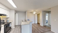 Located at 100 Bent Tree Dr in Daytona Beach, Florida, this one-bedroom, one-bathroom residence offers a well-organized single-floor layout designed for comfortable everyday living. The kitchen serves as a functional centerpiece, featuring white cabinetry, black appliances including a range and refrigerator, light granite-style countertops, and a peninsula with a built-in sink that doubles as a breakfast bar. A skylight-style overhead fixture brightens the cooking area, while wood-style flooring extends through the kitchen and into the adjoining dining and living areas. The living room is accented by a ceiling fan and receives natural light through large windows dressed with vertical blinds. The spacious bedroom is carpeted, includes a ceiling fan, and is lined with multiple windows offering outdoor views of the surrounding greenery. A generous walk-in closet and additional closet storage provide ample organization space. The bathroom is equipped with a full tub-shower combination. A dedicated pantry and utility room further enhance the practicality of this layout, making this a well-rounded residence in a convenient Daytona Beach location.