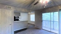 Located along West Highway 98 in Pensacola, Florida, this single-floor residence offers a well-designed open-concept layout that seamlessly connects the kitchen and living areas. The kitchen features dark appliances, including a gas range with an overhead ventilation hood, and is anchored by a peninsula counter with a pass-through opening that looks directly into the main living space — an ideal configuration for both everyday living and entertaining.

The living area is finished with plush carpeting and benefits from abundant natural light streaming in through a large window fitted with horizontal blinds. A ceiling fan with an integrated light fixture is centrally positioned overhead, providing both comfort and illumination. The textured ceiling adds a classic architectural touch throughout the space.

One of the standout features of this unit is the sliding glass door that opens onto a private balcony, offering serene views of the surrounding greenery. The combination of the window and the glass door ensures the living space feels bright and connected to the outdoors. Clean, neutral-toned walls and tasteful flooring transitions between the kitchen and living areas round out this functional and inviting single-floor home.