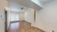 This two-floor space is defined by its striking vaulted ceilings in the main living area, which soar upward and are complemented by a modern brass ceiling fan and recessed lighting. Wood-look flooring runs consistently throughout, lending warmth and visual continuity across both levels. An entry door with a sidelight panel introduces natural light into the entryway, where stairs connect the two floors.

The kitchen is designed in a galley configuration, featuring white cabinetry, dark granite countertops, a mosaic tile backsplash, and a full suite of stainless steel appliances including a refrigerator, range, and over-the-range microwave. A window above the sink provides additional natural light.

Bedrooms are well-proportioned, each offering wood-look flooring and large windows with blinds. The primary bedroom includes two closets and direct access to an en-suite bathroom appointed with a vessel sink, dark granite countertop, white cabinetry, and a framed mirror. A second bathroom features matching granite counters, white cabinetry, and a tub-shower combination with large-format marble-style tile surround. The overall aesthetic is clean, modern, and cohesive throughout.