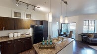 Located at 5000 N Mall Way in Flagstaff, Arizona, this single-floor residence offers a well-designed, contemporary living experience. The open-concept kitchen serves as the heart of the home, featuring dark wood cabinetry, granite-style countertops, a double-basin sink set into a peninsula island, and black appliances including a full-size refrigerator. Pendant lighting and track lighting illuminate the space, adding both function and style.

The living room is bright and welcoming, with vaulted ceilings, a ceiling fan, and large black-framed windows that invite abundant natural light and views of the surrounding mature trees. Hardwood-style flooring flows throughout the main living areas, complementing the clean, modern aesthetic.

The dining area is positioned adjacent to the kitchen and opens via a sliding glass door to an outdoor space with a stone accent wall, offering a seamless indoor-outdoor connection. Each bedroom features carpeted flooring, large windows with outdoor views, and ample wall space. The full bathroom includes a tub-shower combination with wood-look flooring and a granite-topped vanity. A dedicated in-unit laundry area with a full-size washer and dryer adds everyday convenience to this thoughtfully appointed Flagstaff residence.