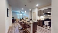 This thoughtfully designed 1-bedroom, 1-bathroom residence offers a single-level open-concept floor plan that seamlessly connects the kitchen, dining, and living areas. The kitchen is a standout feature, showcasing dark cabinetry, granite countertops, a large center island with an undermount sink and pendant lighting, a subway tile backsplash, and a full suite of stainless steel appliances. Bar-height seating at the island provides a casual dining option alongside the open layout.

The living room is bright and welcoming, featuring wood-style plank flooring, a ceiling fan, and a set of French doors that invite natural light and offer access to the outdoors. A built-in desk nook provides a convenient workspace tucked neatly between the living and kitchen areas.

The bedroom is a calm, neutral retreat with a large window that fills the space with natural light, plush carpeting, and ample room for generous furnishings. The bathroom is finished to a high standard with dark wood cabinetry, a granite-top vanity, a large framed mirror, and a walk-in shower. The clean, neutral palette throughout creates a cohesive and modern aesthetic that is both functional and stylish.