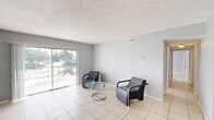 Located at 401 Executive Center Drive in West Palm Beach, Florida, this single-floor, two-bedroom, two-bathroom residence offers a practical and cohesive layout throughout. Light-toned ceramic tile flooring runs consistently across all rooms, contributing to a clean, unified aesthetic.

The living room is a bright and open space anchored by large sliding glass doors that frame outdoor views and allow abundant natural light to fill the room. A textured ceiling and soft gray walls are present throughout the unit, lending a neutral, understated tone.

The kitchen features warm wood-toned cabinetry arranged in a U-shaped layout with white countertops, a stainless steel sink, and black appliances including a refrigerator and range. A louvered closet door provides additional storage access nearby.

The spacious primary bedroom includes closet space and connects easily to the hallway corridor. The second bedroom also offers closet storage and a window that brings in natural light. Both rooms maintain the consistent tile flooring and gray wall palette found throughout the unit.

The two bathrooms are finished with neutral beige tile. One features a tub-shower combination with full tile surround, while the other includes a walk-in shower with mosaic tile flooring and a curtained enclosure. A connecting hallway ties all rooms together efficiently.
