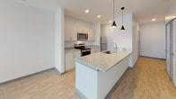 Located at 1525 N Main St in Marion, Indiana, this single-floor unit showcases a contemporary design with a neutral color palette and durable light-toned luxury vinyl plank flooring throughout the main living areas, complemented by plush carpet in the bedrooms.

The kitchen serves as a central highlight, featuring an extended granite-topped island with an integrated sink and pendant lighting overhead. White cabinetry lines the walls, paired with matching granite countertops and a full suite of stainless steel appliances, including a range, microwave, refrigerator, and dishwasher. Recessed lighting ensures a bright, functional workspace.

The living area is generously proportioned, offering a comfortable and open feel. Large windows allow natural light to fill the space, and a ceiling fan adds both style and utility to the room.

The bedroom is a well-sized, carpeted retreat with direct access to a dedicated walk-in closet featuring built-in shelving for organized storage.

The bathroom is finished with the same attention to detail found throughout the unit, including a granite-topped vanity with an undermount sink, a full soaking tub with shower, and coordinating light wood-tone flooring. The overall ambiance is clean, modern, and move-in ready.