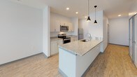 Located at 1525 N Main St in Marion, Indiana, this single-floor unit showcases a contemporary design with a neutral color palette and durable light-toned luxury vinyl plank flooring throughout the main living areas, complemented by plush carpet in the bedrooms.

The kitchen serves as a central highlight, featuring an extended granite-topped island with an integrated sink and pendant lighting overhead. White cabinetry lines the walls, paired with matching granite countertops and a full suite of stainless steel appliances, including a range, microwave, refrigerator, and dishwasher. Recessed lighting ensures a bright, functional workspace.

The living area is generously proportioned, offering a comfortable and open feel. Large windows allow natural light to fill the space, and a ceiling fan adds both style and utility to the room.

The bedroom is a well-sized, carpeted retreat with direct access to a dedicated walk-in closet featuring built-in shelving for organized storage.

The bathroom is finished with the same attention to detail found throughout the unit, including a granite-topped vanity with an undermount sink, a full soaking tub with shower, and coordinating light wood-tone flooring. The overall ambiance is clean, modern, and move-in ready.