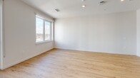Located at 22 Via Toscana in Salem, NH, this efficiently designed single-floor unit offers a clean, modern aesthetic throughout. The open-concept kitchen and living area form the heart of the space, bathed in natural light from large windows and a sliding glass door that opens to a private balcony overlooking the surrounding community. Light wood-tone flooring runs continuously throughout, enhancing the bright and airy feel.

The kitchen is well-appointed with white shaker-style cabinetry featuring matte black hardware, a decorative tile backsplash, light quartz countertops, and a full suite of stainless steel appliances including a refrigerator, range, microwave, and dishwasher. Open shelving adds a contemporary touch to the kitchen design.

The living area is open and versatile, with crisp white walls, recessed lighting, and ample natural light creating a welcoming atmosphere. The bathroom features neutral tile flooring, a tiled tub-shower combination with a chrome shower rod, and clean white fixtures throughout. The entryway provides convenient access to all areas of the unit, with interior doors finished in a modern flat-panel style with matte black hardware that complements the overall design palette.
