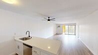 This well-designed 1-bedroom, 1-bathroom unit offers a clean, modern aesthetic throughout its thoughtfully organized single-floor layout. The open-concept living and kitchen area forms the heart of the space, featuring light wood-tone flooring, crisp white walls, and a ceiling fan that enhances the bright, airy feel. A sliding glass door floods the living area with natural light and provides access to an outdoor balcony with views of surrounding greenery.

The kitchen is outfitted with stainless steel appliances, including a gas range, over-the-range microwave, and refrigerator. White shaker-style cabinetry — including a floor-to-ceiling pantry cabinet — and light quartz countertops contribute to a clean, contemporary look. A peninsula countertop connects the kitchen to the living area, offering additional prep and seating space.

The bedroom is a comfortable size, featuring warm wood-tone flooring, a large window with outdoor views, and a wide sliding-door closet providing ample storage. The hallway connects the main living areas to the bathroom and includes additional cabinetry.

The bathroom is finished with dark tile flooring, a white vanity with under-cabinet storage, and a full shower-tub combination. Clean lines and neutral tones carry the cohesive design language throughout the entire unit.