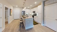 This thoughtfully designed single-floor residence combines contemporary finishes with functional living spaces throughout. The kitchen serves as a central highlight, featuring crisp white shaker cabinetry, light granite countertops, a glass tile backsplash, and a full suite of stainless steel appliances including a gas range, built-in microwave, and refrigerator. A large central island with seating provides additional prep space and a casual dining option, while pendant lighting adds a polished touch overhead. Light wood-look flooring flows through the main living areas, lending a clean, cohesive aesthetic. The bedrooms are generously proportioned, each offering plush carpeting, large windows that invite natural light and outdoor views of lush greenery, and neutral tones that create a calm, restful atmosphere. The bathrooms are well-appointed with granite-topped vanities, white cabinetry, and wood-look tile flooring. One bathroom provides direct access to a spacious walk-in closet with built-in shelving and hanging storage, while another features a soaking tub with a shower combination. Throughout the space, a consistent palette of soft neutrals, clean lines, and quality finishes creates an inviting and move-in-ready environment.