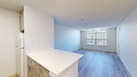 Located at Providence Village Drive in Sterling, Virginia, this one-bedroom, one-bathroom residence offers a well-organized single-floor layout designed for comfortable everyday living. The open-concept living and dining area is bright and airy, anchored by light-toned hardwood-style flooring that runs throughout the space. A standout architectural feature is the large arched window in the living area, which floods the room with natural light and frames views of surrounding trees, creating a warm and inviting atmosphere.

The kitchen is separated from the main living area by a peninsula with a crisp white stone countertop and gold-accented cabinetry, providing both functional workspace and a natural visual divider. A tile backsplash adds a subtle decorative touch. A private balcony extends the living space outdoors, offering a pleasant retreat.

The bedroom is a comfortable, well-proportioned room featuring its own large window with treetop views and a double-door closet with gold hardware. An additional closet elsewhere in the residence provides further storage. The bathroom is clean and modern, equipped with a walk-in shower featuring grab bars, built-in niches, and a bench — a thoughtfully accessible design. Textured ceilings are present throughout, adding subtle architectural character to this neatly appointed home.