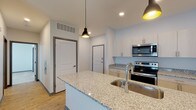 Located at 1525 N Main Street in Marion, Indiana, this single-floor unit offers a clean, modern aesthetic with thoughtfully selected finishes throughout. The kitchen serves as a central highlight, showcasing granite countertop surfaces, crisp white upper cabinetry, and a full suite of stainless steel appliances including a range, microwave, refrigerator, and dishwasher. A spacious island with an integrated sink and pendant lighting above adds both functionality and visual appeal. Light wood-tone luxury vinyl plank flooring runs through the kitchen and main living areas, creating a warm, cohesive feel. The layout, as seen in the floor plan, connects the kitchen and living areas in an open, accessible arrangement. The bedrooms feature plush carpeting, ceiling fans with lighting, and windows fitted with blinds that allow for natural light while maintaining privacy — one bedroom benefits from a dual-window configuration. The bathroom is finished with the same granite countertop detail seen in the kitchen, complemented by warm wood-tone cabinetry, a full tub-shower combination, and matching luxury vinyl plank flooring. Recessed lighting and a neutral white-and-gray palette throughout the unit contribute to a bright, contemporary atmosphere that feels clean and move-in ready.