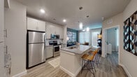 This single-floor residence showcases a thoughtfully designed open-concept layout connecting the kitchen, dining, and living areas. The kitchen is a standout feature, offering white or gray shaker-style cabinetry, granite countertops, and a full suite of stainless steel appliances including a refrigerator, electric range, and microwave. A central island with an undermount sink and bar seating serves as both a functional workspace and casual dining area, illuminated by sleek pendant lighting overhead. Light wood-look flooring flows consistently throughout the space, enhancing the bright and cohesive aesthetic.

The living area benefits from natural light streaming through large windows dressed with blinds and sheer curtains, creating an airy, welcoming atmosphere. An accent wall adds a subtle pop of color, contributing visual depth to the open layout.

The bedrooms are comfortably sized, each featuring windows with natural light, wood-look flooring, and ample closet access. The bathroom is clean and well-appointed, with granite-topped vanity cabinetry, wood-look tile flooring, and efficient use of space. Overall, the residence presents a modern, neutral palette with contemporary finishes throughout.