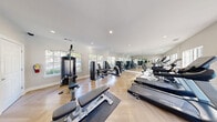 Located at 2334 Fuller Way in Tucker, GA, this well-appointed fitness center offers a comprehensive workout facility designed to support a wide range of exercise routines. The single-room space is thoughtfully laid out to maximize functionality, featuring light-toned herringbone hardwood floors that lend a polished, upscale aesthetic throughout.

Large, multi-pane windows line the walls, flooding the interior with abundant natural light and offering pleasant views of a neighboring outdoor pool area. Full-length mirrors along one wall visually expand the space and allow users to monitor their form during workouts.

Recessed lighting in the bright white ceiling provides consistent, even illumination throughout the room. The cardio section is well-stocked with Spirit-brand treadmills, elliptical trainers, and stationary bikes, all positioned to take advantage of the natural light and views. The strength training area features a variety of resistance machines from True and other brands, along with free weights including a full dumbbell rack, adjustable benches, and a multi-station cable machine. Exercise mats are also available for floor-based workouts.

The space is accessed through a glass-paned door and maintains a clean, neutral color palette of whites and soft grays, creating a bright and motivating environment well-suited for daily fitness activities.