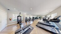 Located at 2334 Fuller Way in Tucker, GA, this well-appointed fitness center offers a comprehensive workout facility designed to support a wide range of exercise routines. The single-room space is thoughtfully laid out to maximize functionality, featuring light-toned herringbone hardwood floors that lend a polished, upscale aesthetic throughout.

Large, multi-pane windows line the walls, flooding the interior with abundant natural light and offering pleasant views of a neighboring outdoor pool area. Full-length mirrors along one wall visually expand the space and allow users to monitor their form during workouts.

Recessed lighting in the bright white ceiling provides consistent, even illumination throughout the room. The cardio section is well-stocked with Spirit-brand treadmills, elliptical trainers, and stationary bikes, all positioned to take advantage of the natural light and views. The strength training area features a variety of resistance machines from True and other brands, along with free weights including a full dumbbell rack, adjustable benches, and a multi-station cable machine. Exercise mats are also available for floor-based workouts.

The space is accessed through a glass-paned door and maintains a clean, neutral color palette of whites and soft grays, creating a bright and motivating environment well-suited for daily fitness activities.