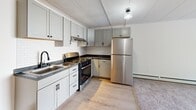 Located at 101 Oaklawn Ave in Cranston, Rhode Island, this one-bedroom, one-bathroom unit offers a thoughtfully organized single-floor layout. The combined living, dining, and kitchen area forms the heart of the home, where light hardwood-style flooring flows through the kitchen and transitions into carpet in the living space. The kitchen is a standout feature, outfitted with soft gray shaker-style cabinetry, a classic white subway tile backsplash, dark countertops, a stainless steel sink, and a full suite of stainless steel appliances including a gas range and refrigerator. Sliding glass doors in the living area invite natural light and provide access to an outdoor balcony view. The bedroom is a comfortable, carpeted retreat with neutral white walls, a window with blinds overlooking greenery, and baseboard heating. Two closets provide convenient storage throughout the unit. The bathroom features a clean, all-white aesthetic with a tub and shower combination, hexagonal tile flooring, and a vanity with ample counter space. The overall palette of whites and neutrals creates a bright, clean ambiance throughout this well-appointed Cranston residence.