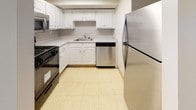 Located at 808 Memorial Dr in Cambridge, MA, this single-floor unit offers a straightforward and functional layout across several well-defined spaces. The living area is generously sized, featuring neutral wall-to-wall carpeting and a large sliding glass door that opens to a balcony, allowing natural light to fill the room and providing views of the surrounding Cambridge landscape.

The kitchen is efficiently arranged in an L-shaped configuration, outfitted with white cabinetry, light countertops, and tile flooring. Stainless steel appliances—including a refrigerator, dishwasher, and microwave—complement a black gas range, creating a practical cooking environment with ample storage.

The bedrooms continue the carpeted flooring and neutral palette, each featuring large windows dressed with vertical blinds that frame outdoor views and invite natural light. The unit includes two bathrooms: one with a full soaking tub and shower, white subway tile surround, and a wood-toned vanity; and a second with mosaic tile flooring, a natural wood-framed window, and clean white walls. Central HVAC with ceiling vents ensures year-round climate control throughout the unit.