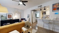 This single-floor residence showcases a thoughtfully curated boho-modern aesthetic throughout its well-appointed layout. The living area is anchored by polished concrete floors, a ceiling fan, and an arched doorway that connects seamlessly to the kitchen. Eclectic décor—including a statement macramé wall piece, a rich caramel leather sofa, and a plush navy velvet accent chair—lends warmth and personality to the space. A sleek dark media console and a round acrylic coffee table complete the inviting sitting area, which is bathed in natural light from sheer-curtained windows.

The kitchen features white shaker cabinetry with matte black hardware, a geometric tile backsplash, white quartz countertops, stainless steel appliances, and a standout retro turquoise refrigerator that adds a pop of color. Pendant lighting over the breakfast bar enhances the kitchen's modern-casual character.

The bedroom offers a serene retreat with carpeted floors, a classic black iron bed frame, track lighting, and a large fiddle-leaf fig plant that brings natural life to the room. A dedicated workspace sits beside a sheer-draped window.

The bathroom is clean and contemporary, finished with white shaker vanity cabinetry, quartz countertops, black hardware accents, and an elegant arched mirror above the undermount sink.