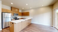 This two-story home offers a clean, contemporary design with thoughtful finishes across both levels. The kitchen is a standout feature, showcasing warm wood-toned cabinetry, crisp white countertops, and a full suite of stainless steel appliances including a refrigerator, electric range, and over-the-range microwave. A peninsula with an integrated sink and breakfast bar overhang creates a natural transition into the adjacent living area, all set atop light hardwood-style flooring that flows throughout the main level.

The staircase, finished with carpet treads and a clean white banister, connects the floors with a neat, practical design. Upstairs, the bedrooms feature plush carpet flooring and windows with blinds that invite natural light and outdoor views. A spacious walk-in closet with built-in shelving and hanging rods provides ample organized storage. The bathroom includes a full tub-shower combination with white surround and brushed nickel fixtures, complemented by wood-style flooring.

The attached garage offers generous space with a concrete floor, automated door opener, and windows above the garage door that allow natural light in. Neutral tones, recessed lighting, and consistent finishes throughout give the home a cohesive, move-in-ready feel.