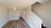 This two-story unit offers a practical and comfortable layout spread across two levels. The main floor features durable wood-look flooring that extends through the living area and kitchen, creating a cohesive and easy-to-maintain surface. The living room is well-lit, benefiting from a sliding glass door that invites natural light and provides outdoor access. A ceiling fan overhead adds both function and comfort to the space.

The kitchen is laid out in a U-shape configuration, equipped with warm wood-toned cabinetry, white appliances including an electric range, refrigerator, and dishwasher, along with a stainless steel sink positioned near a window. Light countertops provide ample workspace throughout.

A staircase leads to the upper level, where both bedrooms are located. Each bedroom features plush carpet flooring, ceiling fans, and windows that allow natural light to filter in. Closet storage is available in each room, with louvered bifold doors visible in the main bedroom area.

The full bathroom includes a tub-shower combination with a white surround and chrome fixtures. A half bathroom is also present, providing added convenience for daily living. Neutral wall tones and textured ceilings are consistent throughout the unit.