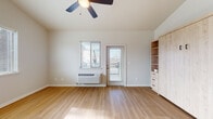 This single-floor unit offers a clean, contemporary design with an open-concept layout that seamlessly connects the kitchen and living areas. Light hardwood-style flooring flows throughout, creating a warm and cohesive aesthetic. The kitchen is well-equipped with stainless steel appliances — including a refrigerator, range, and built-in microwave — complemented by light wood cabinetry and a central island with an integrated sink and dishwasher, providing ample prep and storage space. A window above the kitchen counter allows natural light to filter in, keeping the space bright and airy.

The living area benefits from vaulted ceilings and a ceiling fan with a built-in light fixture, enhancing the sense of openness. A wall-mounted HVAC unit ensures year-round climate comfort. Built-in shelving and cabinetry in natural wood tones offer practical storage solutions. A glass-panel door leads directly to an outdoor deck, extending the living space and bringing in additional natural light.

The bathroom is a standout feature, finished with patterned encaustic-style floor tiles that add a decorative touch to an otherwise clean, neutral palette. The full bath includes a soaking tub and bright white fixtures. A dedicated laundry area is also present within the unit, adding to its everyday functionality.