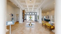 The Camelot at Cinnaminson Harbour clubhouse at 198 Camelot Ct offers a thoughtfully designed community facility spanning a generous single floor. The grand lobby immediately impresses with soaring coffered ceilings, stately white columns, and large-scale chandelier lighting that floods the space with a warm, welcoming glow. Polished tile flooring, a dramatic stone fireplace, and floor-to-ceiling French doors with sheer drapery contribute to an elegant yet approachable atmosphere. Seating areas are arranged throughout the open lobby, providing comfortable spaces for socializing or relaxing. A dedicated conference room features wainscoting, pendant lighting, and a large dark conference table surrounded by upholstered chairs, making it well-suited for meetings or community gatherings. Abstract artwork and tall windows with natural light complete the professional yet inviting ambiance of the room. A compact business nook offers a built-in desk and storage cabinetry, ideal for focused individual work. The fitness center is a standout feature, boasting high arched windows that bathe the room in natural light, hardwood-style flooring, ceiling fans, and an extensive array of cardio and strength-training equipment. Together, these spaces create a versatile and polished community hub designed to meet a variety of residential needs.