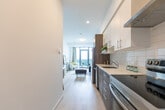 This well-appointed one-bedroom, one-bathroom residence in California offers a smart, efficient layout across a single floor. The open-concept living and kitchen area is anchored by light hardwood flooring and crisp white walls that create a bright, airy atmosphere throughout. The modern kitchen features two-tone cabinetry — combining warm wood-tone lower cabinets with white upper units — accented by a classic subway tile backsplash, quartz countertops, stainless steel appliances including a refrigerator and dishwasher, and a single-basin sink. The living room is a standout, boasting floor-to-ceiling windows and a glass door that opens to a balcony, framing expansive elevated views of the surrounding landscape and allowing abundant natural light to pour in. The bedroom offers a cozy carpeted retreat with a generous closet and its own set of large windows that showcase the same impressive panoramic views. The bathroom is finished with neutral tile surround and includes a full soaking tub with shower. A dedicated nook near the entryway provides a flexible workspace. Clean lines, contemporary finishes, and elevated views define the overall ambiance of this compact yet functional urban residence.