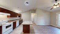 This single-story unit in Aiken, South Carolina offers a thoughtfully arranged layout encompassing a living room, kitchen, bedroom, walk-in closet, bathroom, and hallway. A standout architectural feature is the vaulted ceiling in the kitchen and living area, which adds a sense of openness and volume beyond the unit's modest footprint.

The kitchen is well-appointed with rich dark-brown cabinetry, granite-style countertops, white appliances including a range, dishwasher, and refrigerator, and a freestanding island that provides additional prep and dining space. Light-toned, hardwood-style flooring runs consistently throughout the unit, contributing to a clean, cohesive aesthetic.

The living area benefits from a ceiling fan and a glass-paned exterior door that invites natural light. A large window in the bedroom further enhances brightness, while neutral wall tones create a calm, versatile backdrop. The bedroom includes access to a spacious walk-in closet equipped with wire shelving on three walls for ample storage.

The bathroom features a full tub-shower combo, toilet, vanity, and overhead cabinetry. Overall, the unit presents a functional and efficiently organized living space with consistent finishes throughout.