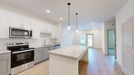 Located at 1485 Fouraker Road in Jacksonville, FL, this well-designed one-bedroom, one-bathroom unit offers a thoughtfully organized single-floor layout. The open-concept kitchen, dining, and living area forms the heart of the home, anchored by a large granite-topped kitchen island illuminated by sleek pendant lighting. The kitchen showcases white upper cabinetry, grey lower cabinets, a white subway tile backsplash, granite countertops, and a full suite of stainless steel appliances including a range, microwave, dishwasher, and refrigerator. Light hardwood-style flooring runs throughout the main living areas, enhancing the bright, airy feel. The living area benefits from natural light through windows and a glass door leading outside. The bedroom features plush carpeting, a ceiling fan, and a window with outdoor views. The full bathroom is well-appointed with a dual-sink granite vanity, white cabinetry, a soaking tub with subway tile surround, and wood-style flooring. A spacious walk-in closet with wire shelving provides ample storage. A dedicated laundry area with an in-unit washer completes this efficiently designed and modern residence.