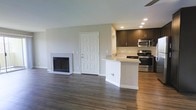 This single-floor space showcases a thoughtfully designed open-concept layout that seamlessly connects the living area and kitchen, creating a sense of spaciousness and ease of flow. The living area is anchored by a clean, white-framed fireplace that adds warmth and a classic focal point to the room. Rich, dark hardwood floors run throughout, providing an elegant contrast to the neutral, light-toned walls and crisp white trim and baseboards.

The kitchen is outfitted with dark espresso-toned cabinetry that offers generous storage, complemented by a light stone countertop that extends into a peninsula with a built-in sink — ideal for casual dining or food preparation. Stainless steel appliances, including a range and an over-the-range microwave, add a modern, polished finish to the culinary space.

Recessed lighting in the kitchen ensures the area is well-lit and functional, while a ceiling fan contributes to comfortable air circulation throughout. The overall ambiance of the space is clean, contemporary, and move-in ready, with a neutral palette that provides a versatile backdrop for a variety of interior design styles.