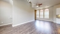 Located at 9600 Gaylord Pkwy in Frisco, TX, this three-story home offers a thoughtfully designed layout spread across multiple levels. The ground floor houses an attached garage with direct interior access, providing secure and convenient parking. The main living level serves as the heart of the home, featuring a combined kitchen and living area with soaring vaulted ceilings and a ceiling fan. Striking arched windows flood the living space with natural light, complementing the rich, dark hardwood-style flooring throughout. The gourmet kitchen is appointed with crisp white cabinetry, granite countertops, a large center island with a built-in cooktop, a sleek stainless steel island range hood, and stainless steel appliances including a French door refrigerator and microwave. A mosaic tile backsplash adds a stylish finishing touch. The upper floor is dedicated to the private bedroom suite, featuring plush carpeting, multiple windows for ample natural light, and a ceiling fan. The suite includes direct access to a walk-in closet outfitted with wire shelving systems and a well-appointed full bathroom featuring large-format tile walls, a soaking tub, and a glass-enclosed walk-in shower with a separate shower pan.