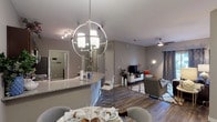 This single-floor residence is designed with a cohesive, modern aesthetic highlighted by neutral gray tones, wood-look flooring, and consistent dark cabinetry throughout. The open-concept layout connects the kitchen, dining, and living areas seamlessly. A striking spherical chrome chandelier anchors the dining space, while the kitchen features rich dark-espresso cabinetry, granite countertops, a decorative tile backsplash, and a full suite of stainless steel appliances. A granite-topped breakfast bar provides additional seating and further integrates the kitchen with the living areas.

The living room offers a relaxed, comfortable atmosphere with a ceiling fan, patterned drapery, and sliding glass door access to the exterior. A flexible secondary room functions as a home office or den, complete with a ceiling fan and natural light from a window.

The bedroom is carpeted and tranquil, featuring a ceiling fan and a window with blinds and coordinating drapes. Two bathrooms serve the unit — one with a tub-shower combination and large-format tile surround, and another with a walk-in shower finished in matching gray tile — both offering granite vanity countertops and dark cabinetry.

A dedicated laundry room houses a full-size washer and dryer alongside additional cabinetry and granite countertops, adding functional convenience to the space.