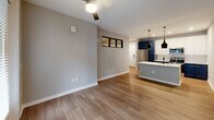 Located at 1711 Commonwealth Ave in Charlotte's 28205 zip code, this well-appointed single-story unit offers a thoughtfully designed open-concept layout. The combined living, dining, and kitchen area serves as the heart of the home, featuring warm wood-look flooring, neutral gray walls, and a ceiling fan that enhances comfort and airflow. The kitchen stands out with bold navy cabinetry, white upper cabinets, a striking quartz waterfall island with an undermount sink and matte black faucet, and stainless steel appliances. Sleek black pendant lights hang above the island, adding a modern, industrial touch. Natural light filters in through double glass patio doors and an interior clerestory window that connects the bedroom to the living space, creating an airy, connected feel. The bedroom is a calm retreat with wood-look flooring, a ceiling fan, and a horizontal black-framed window. It connects directly to the bathroom and a dedicated closet. The bathroom is finished with white cabinetry, quartz countertops, black hardware accents, a tiled walk-in shower with glass door, and a double-door closet for ample storage. An in-unit laundry area and a private patio complete this efficiently designed home.