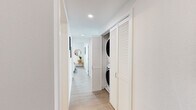 Located in Berkeley, CA, this contemporary single-floor residence offers a thoughtfully designed layout with clean lines and a bright, modern aesthetic throughout. Light wood-tone flooring flows seamlessly across the entire space, complementing the crisp white walls and recessed lighting.

The living room is a standout feature, showcasing floor-to-ceiling black-framed windows that flood the space with natural light and frame sweeping views of the surrounding Berkeley cityscape and beyond. The open layout comfortably accommodates a full seating arrangement, and the airy atmosphere is enhanced by the elevated vantage point.

The kitchen is sleek and functional, outfitted with high-gloss white cabinetry extending to the ceiling, stainless steel appliances, a tile backsplash, and a peninsula with counter seating. A distinctive circular porthole window adds a unique architectural touch.

The bedrooms are generously sized and well-lit, each with large windows offering city views. The primary bedroom includes direct access to a full bathroom and a dedicated closet. Both bathrooms are finished in a clean, minimalist style with white soaking tubs, modern vanities, and wood-look flooring.

A hallway laundry closet with a stacked washer and dryer unit adds everyday convenience. Throughout, the space maintains a cohesive, contemporary feel suited to modern urban living.