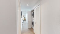 Located in Berkeley, CA, this contemporary single-floor residence offers a thoughtfully designed layout with clean lines and a bright, modern aesthetic throughout. Light wood-tone flooring flows seamlessly across the entire space, complementing the crisp white walls and recessed lighting.

The living room is a standout feature, showcasing floor-to-ceiling black-framed windows that flood the space with natural light and frame sweeping views of the surrounding Berkeley cityscape and beyond. The open layout comfortably accommodates a full seating arrangement, and the airy atmosphere is enhanced by the elevated vantage point.

The kitchen is sleek and functional, outfitted with high-gloss white cabinetry extending to the ceiling, stainless steel appliances, a tile backsplash, and a peninsula with counter seating. A distinctive circular porthole window adds a unique architectural touch.

The bedrooms are generously sized and well-lit, each with large windows offering city views. The primary bedroom includes direct access to a full bathroom and a dedicated closet. Both bathrooms are finished in a clean, minimalist style with white soaking tubs, modern vanities, and wood-look flooring.

A hallway laundry closet with a stacked washer and dryer unit adds everyday convenience. Throughout, the space maintains a cohesive, contemporary feel suited to modern urban living.